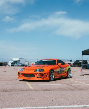 Vivid orange Toyota Supra displayed at an outdoor automotive event on a sunny day.