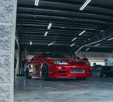 Red Nissan GTR R34 parked indoors with overhead lighting.