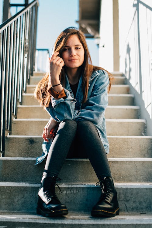 Woman In Blue Denim Jacket And Black Pants Sitting On Stairs