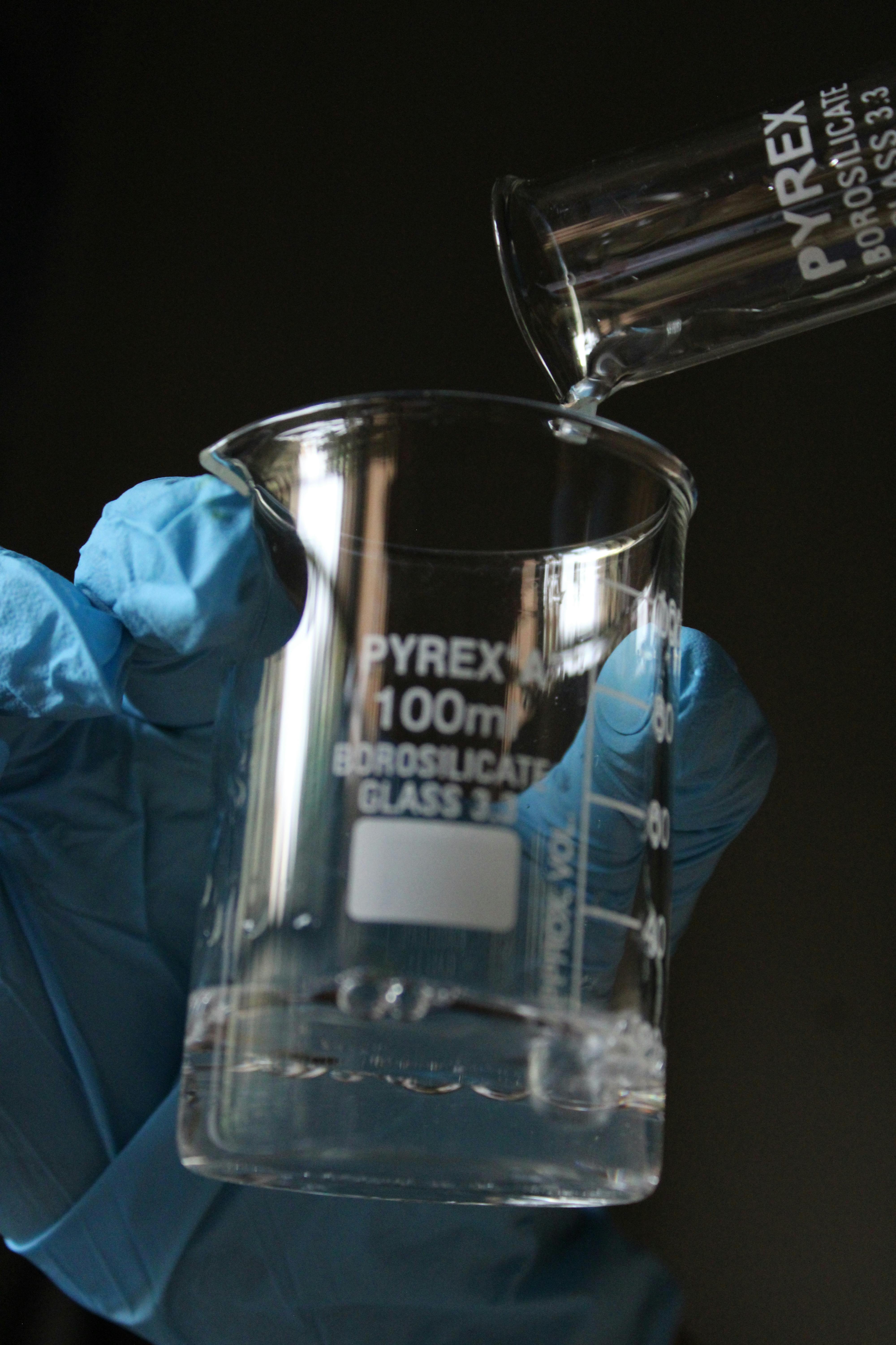 Close-up of a 100ml Pyrex beaker with liquid pouring in for a lab experiment.