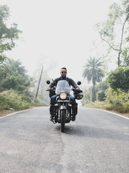在印度，一名摩托车手正沿着一条绿树成荫、风景如画的道路行驶