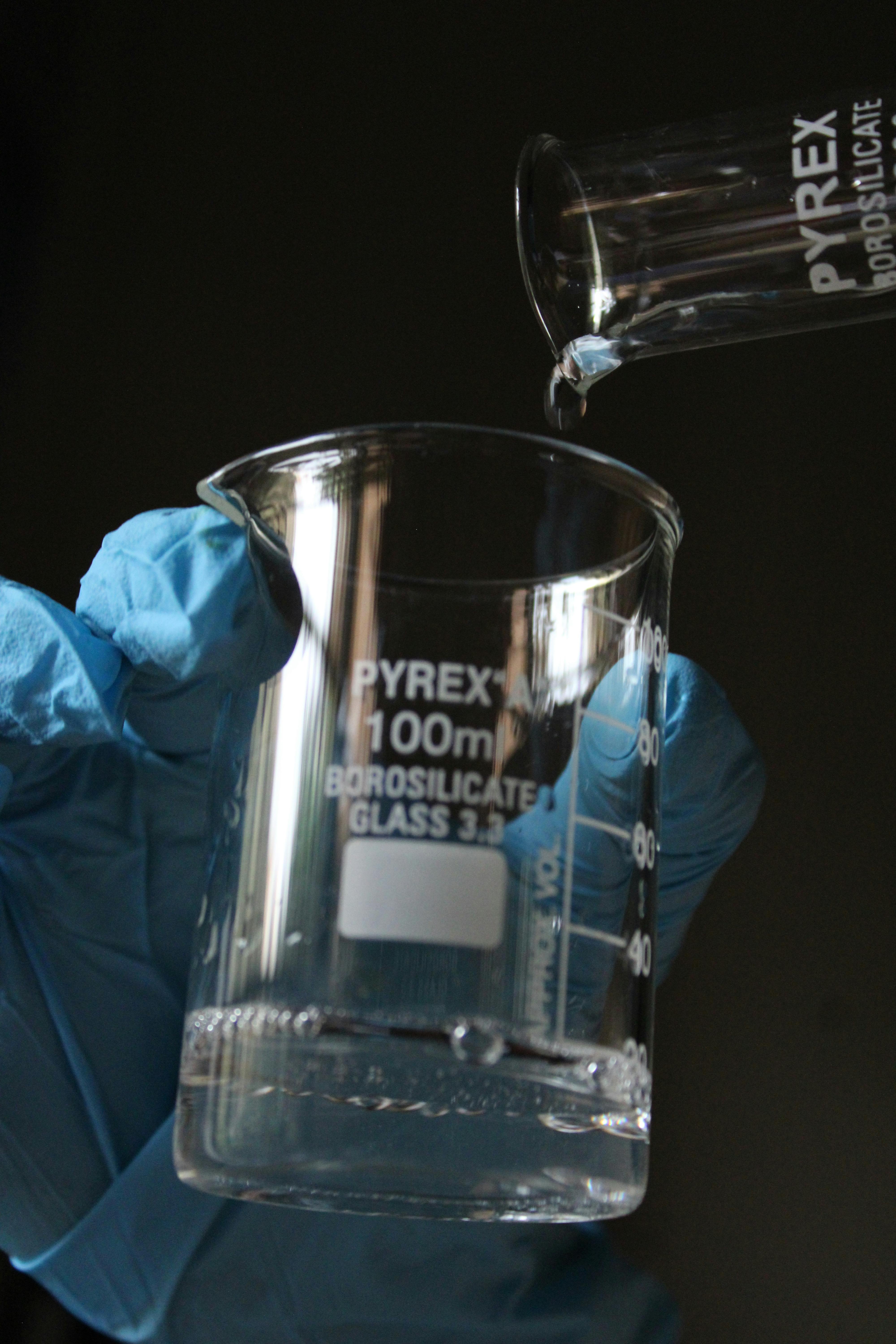 Scientist wearing gloves pours liquid into a glass beaker.
