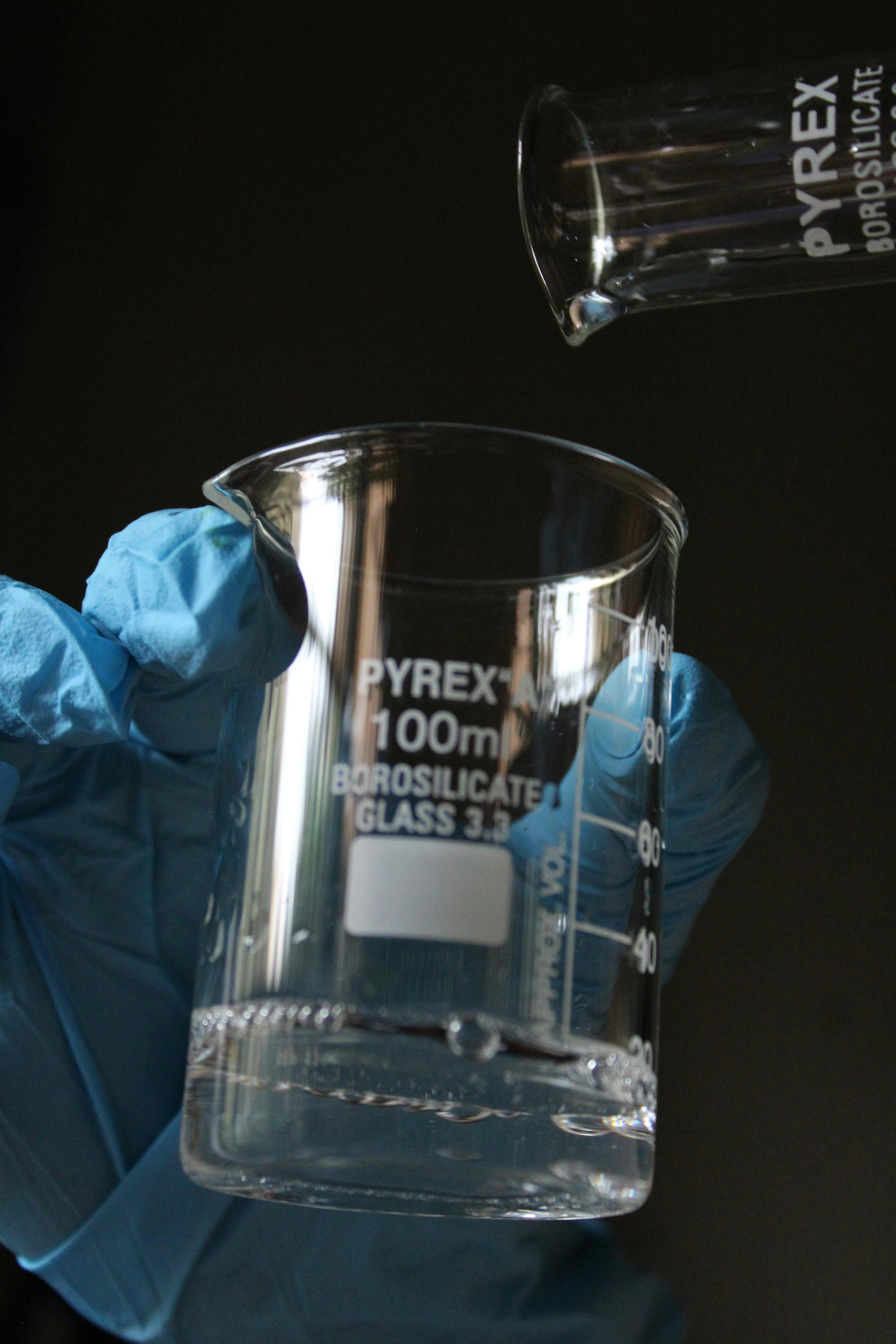 Close-up of a scientist's hand holding a Pyrex beaker in a laboratory setting.
