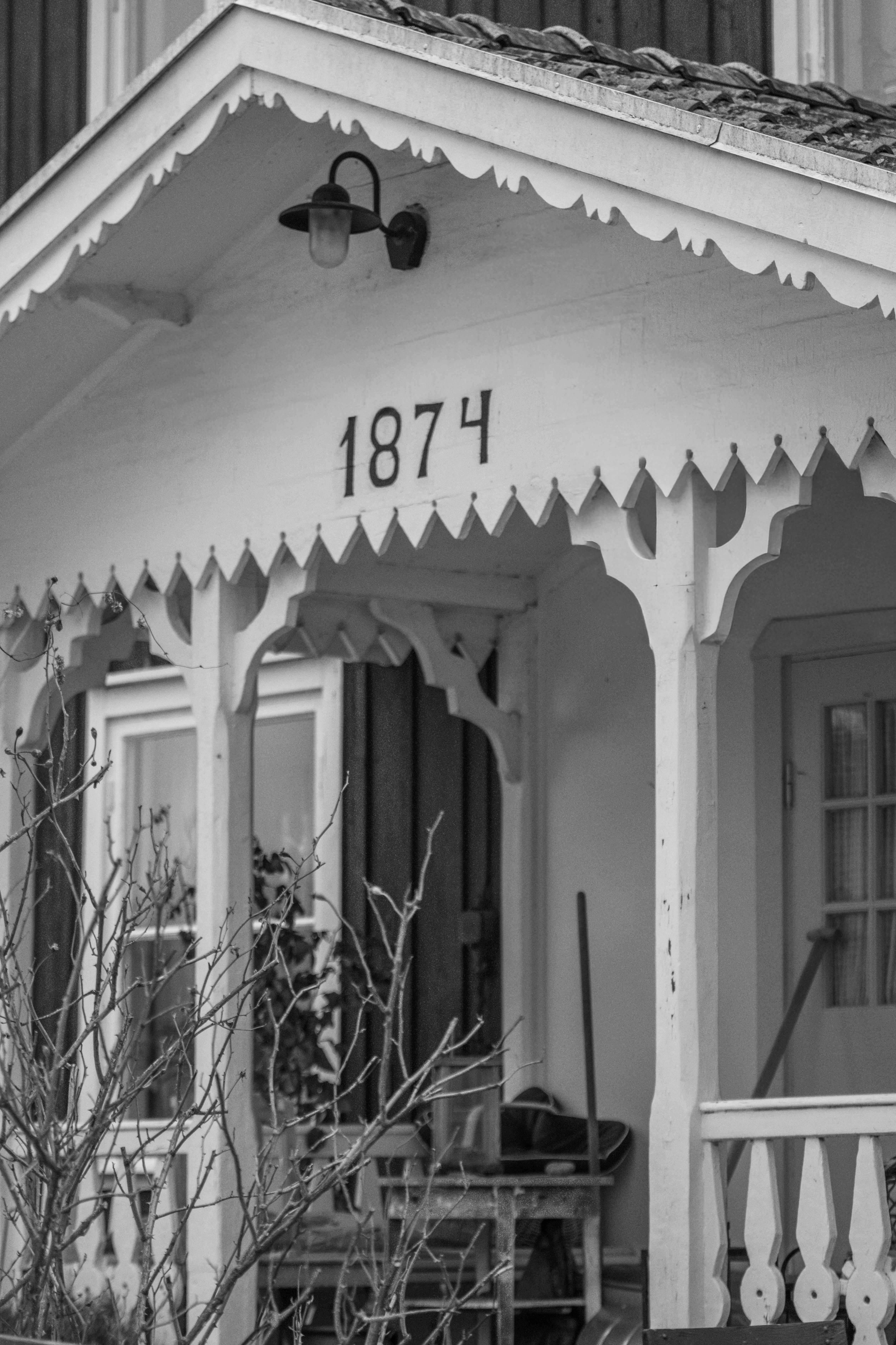 A historic Swedish porch from 1874, showcasing classic 19th-century wooden architecture in a black and white tone.