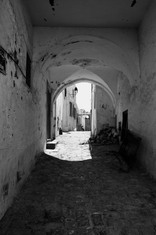 Free A dramatic black and white photo of an old town alleyway with arched passages. Stock Photo