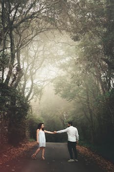 一对情侣手牵着手，走在雾蒙蒙的森林道路上，显得浪漫而团结
