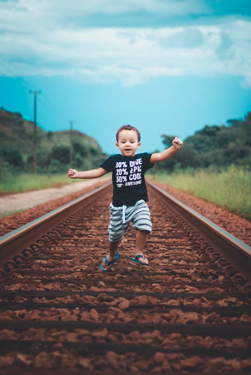Boy In Black T-shirt And Shorts Running On Train Tracks