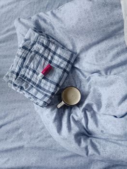 A cup of coffee on a bed with pajamas and lip balm, creating a cozy morning vibe.