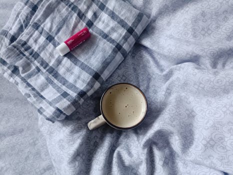 A warm cup of coffee with skincare on a cozy plaid blanket, perfect for a relaxing morning aesthetic.