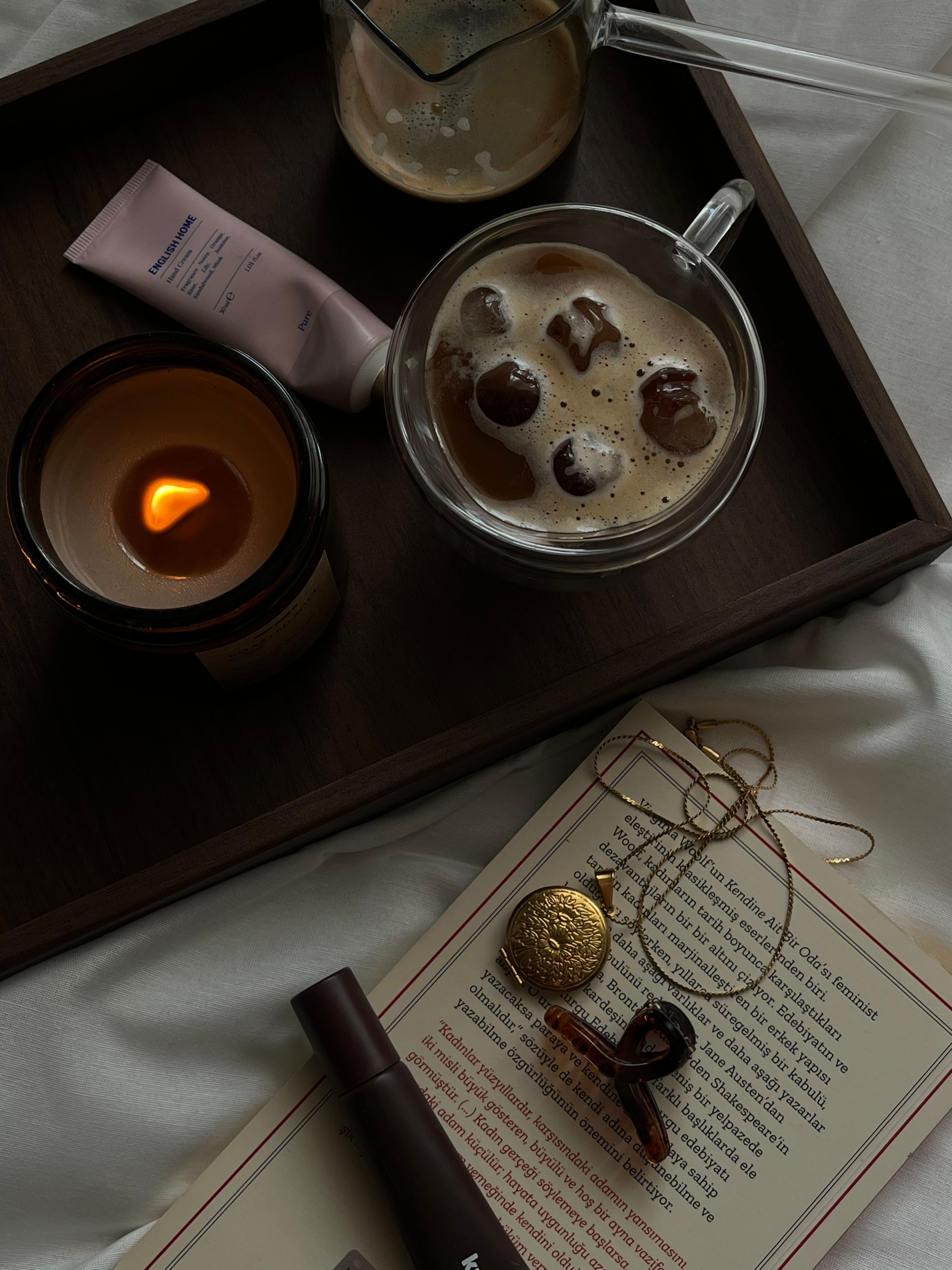 Warm and cozy setup with coffee, candle, and luxury accessories on a wooden tray for a relaxing morning.