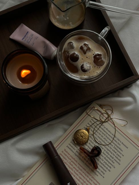 Warm and cozy setup with coffee, candle, and luxury accessories on a wooden tray for a relaxing morning.