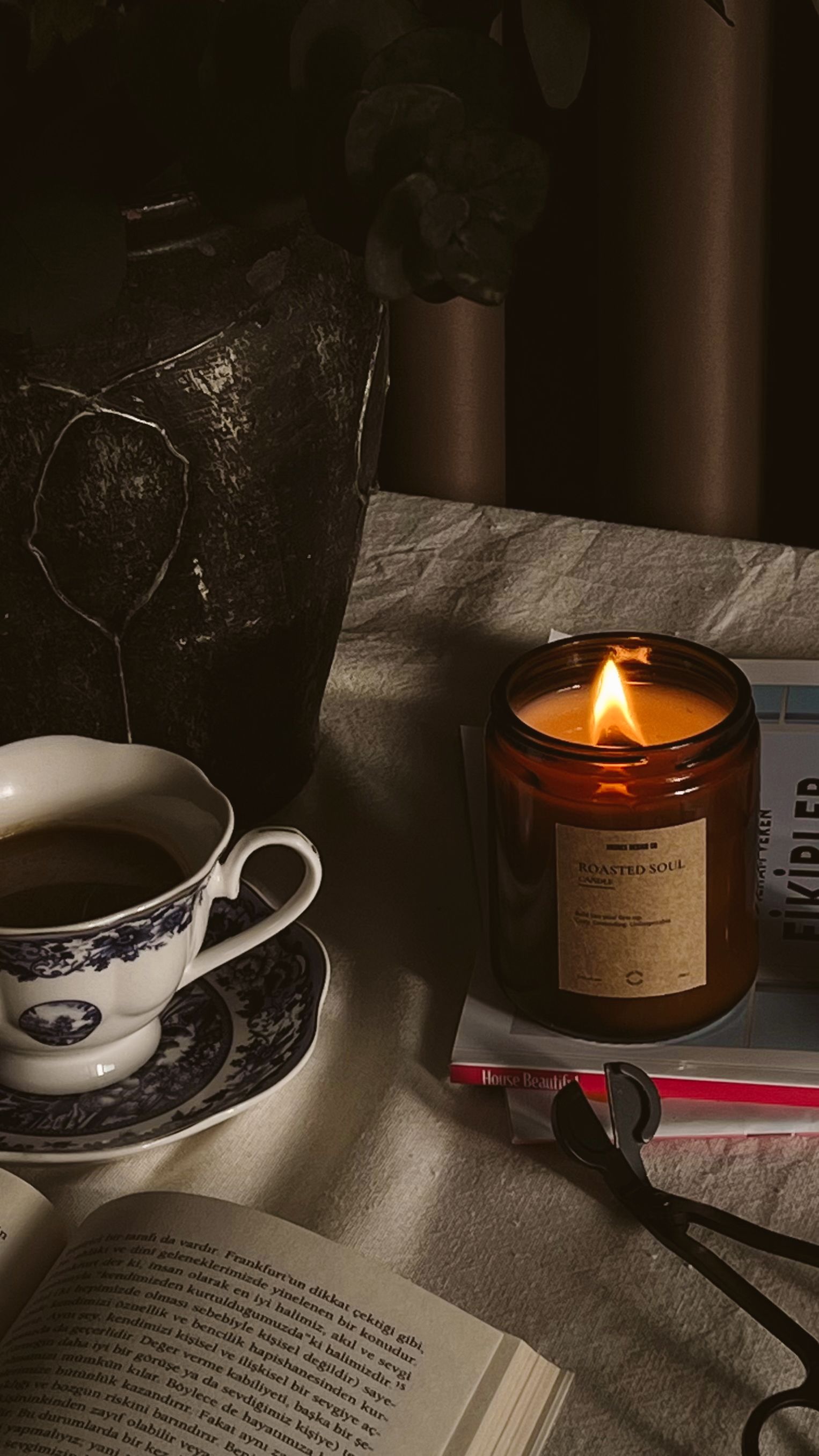 Ambient evening still life featuring a lit candle, coffee, and books on a table.