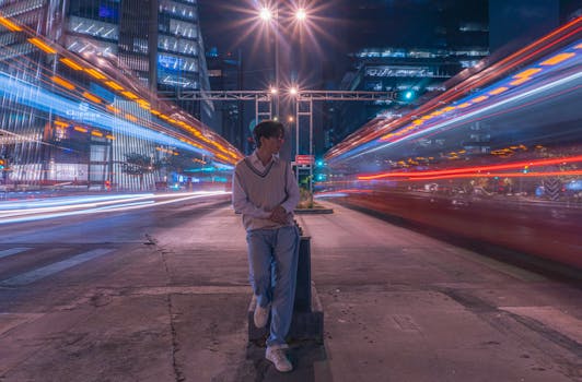 Young man stands in vibrant cityscape with dynamic light trails at night, creating an urban atmosphere.