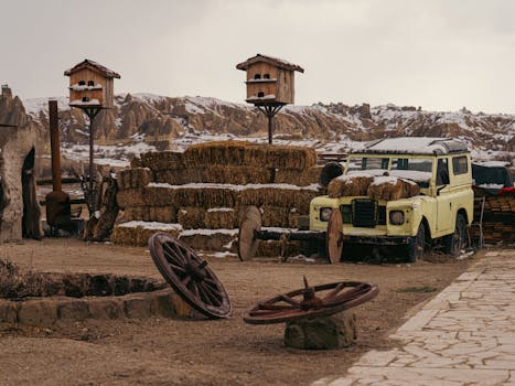 Rustic landscape in Cappadocia featuring an old Land Rover by a haystack and wooden birdhouses.