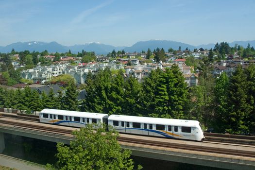 Vancouver SkyTrain traversing suburban area with scenic mountain backdrop.