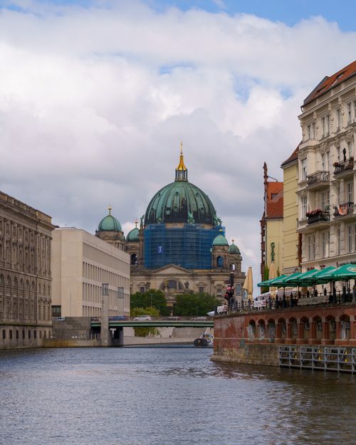 Free Picturesque scene of Berlin Cathedral and surrounding architecture along a canal under a cloudy sky. Stock Photo