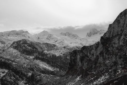 Scenery view of gray mounts with uneven surface partially covered with fog and snow under cloudy sky in winter