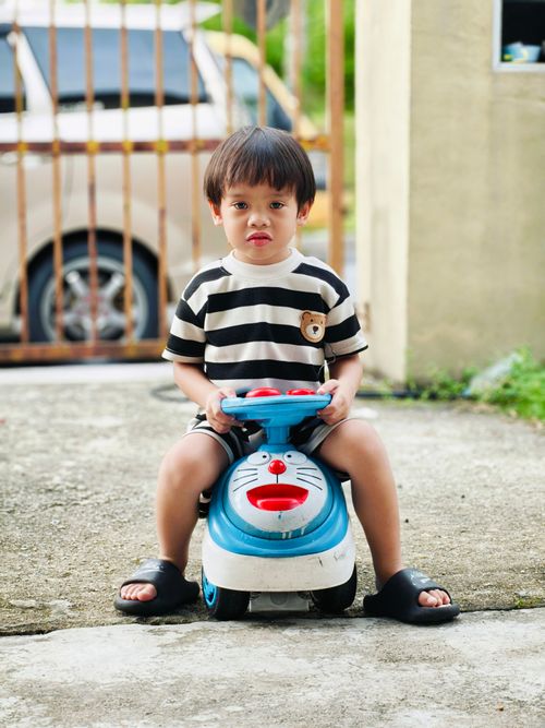 Free Young boy in striped shirt rides a blue toy car outside in Uzbekistan. Stock Photo