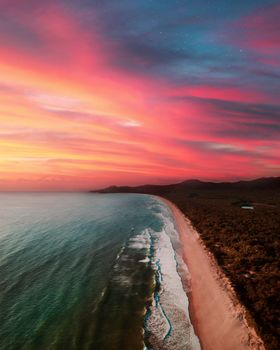 Breathtaking aerial view of a beach with vibrant sunset skies and calm waves.
