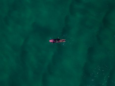 Drone shot capturing a surfer paddling on a surfboard in the serene ocean waters.