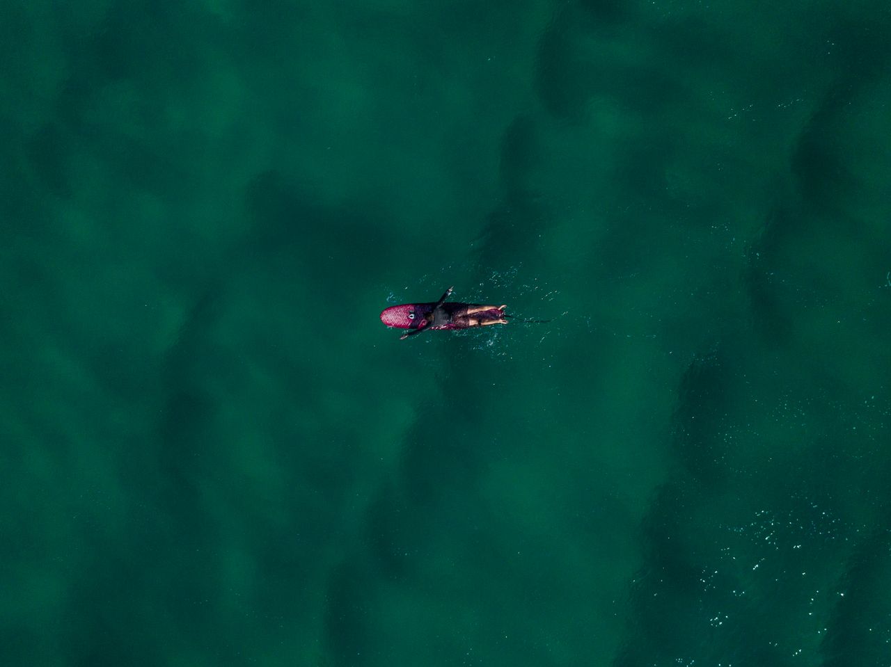 drone shot capturing a surfer paddling on a surfboard in the serene oc