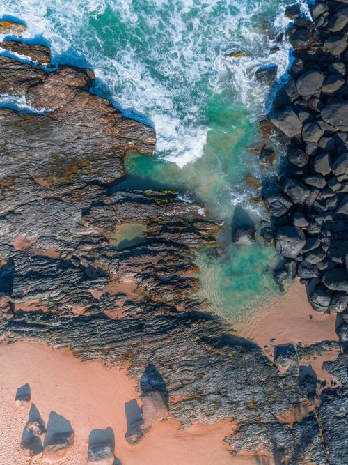 Free Drone captures stunning aerial view of a rocky seashore with turquoise waves crashing over rocks. Stock Photo