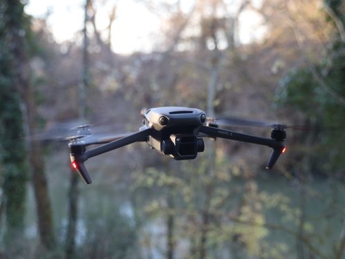 Free DJI Mavic 3 drone in flight over scenic forested area. Stock Photo