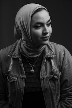 Artistic black and white portrait of a woman in a hijab and denim jacket, exuding mystery and style.