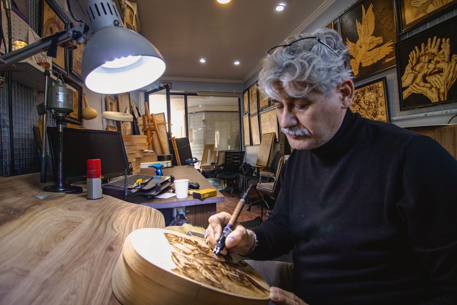 Artisan engaged in detailed wood engraving in a well-lit workshop filled with wooden art pieces.