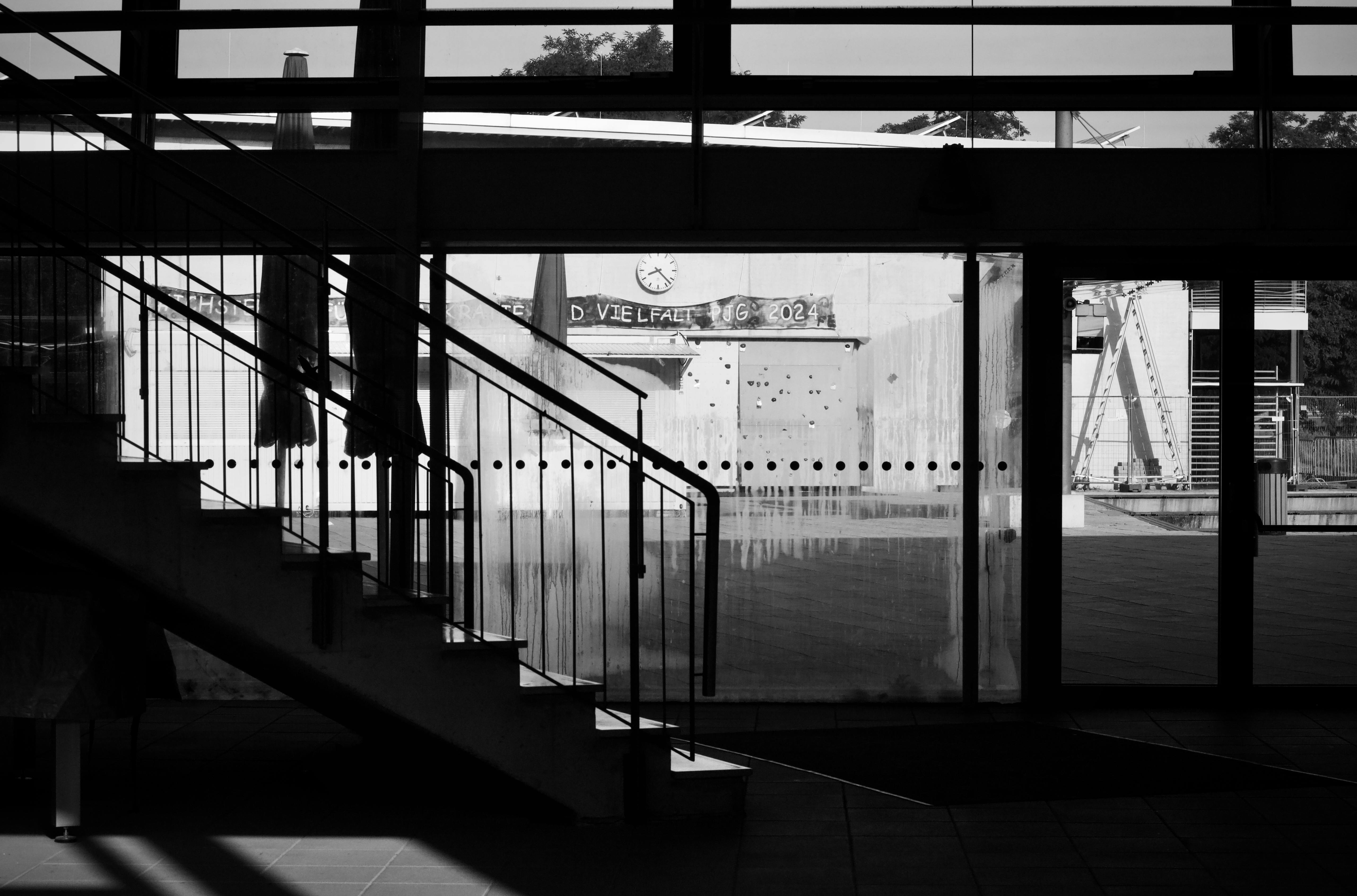 Gratis Una scena minimalista in bianco e nero in un interno con una scala e finestre in vetro che proiettano ombre geometriche. Foto a disposizione