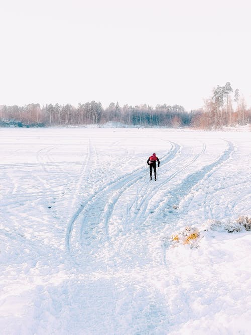 Free Person in Red Jacket and Blue Pants Walking on Snow Covered Ground Stock Photo