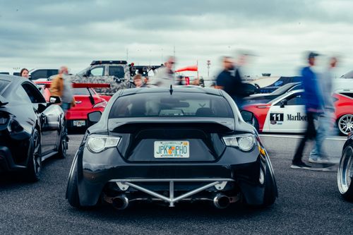 Free Modified cars on display at a lively car show with people in motion, highlighting automotive culture. Stock Photo
