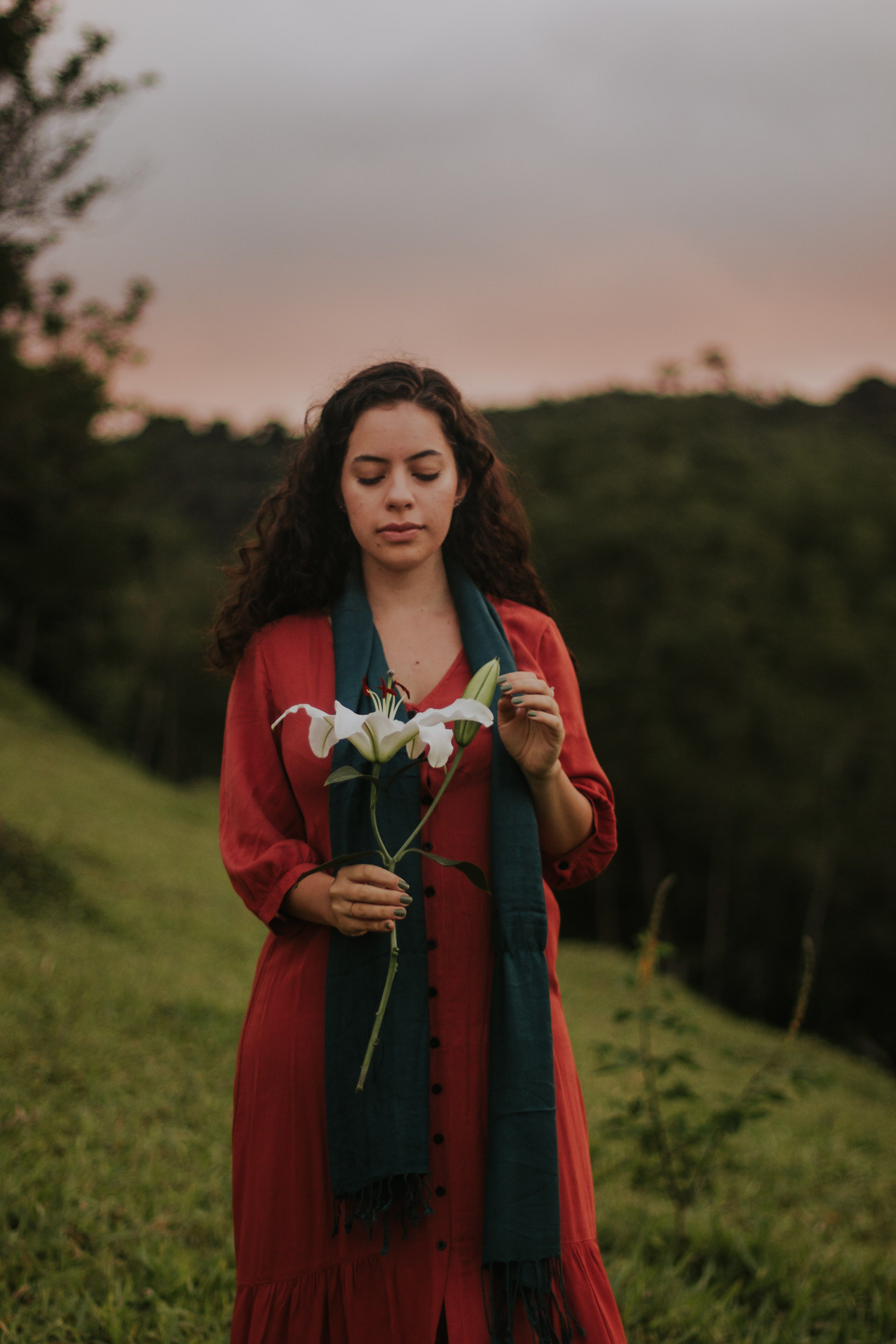 Serene woman in red dress holding a lily outdoors at sunset, evoking tranquility.