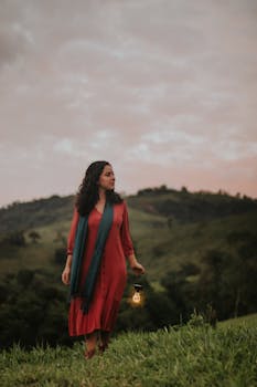 Young woman in scenic landscape holding a glowing lantern at dusk, evoking a sense of serenity and adventure.