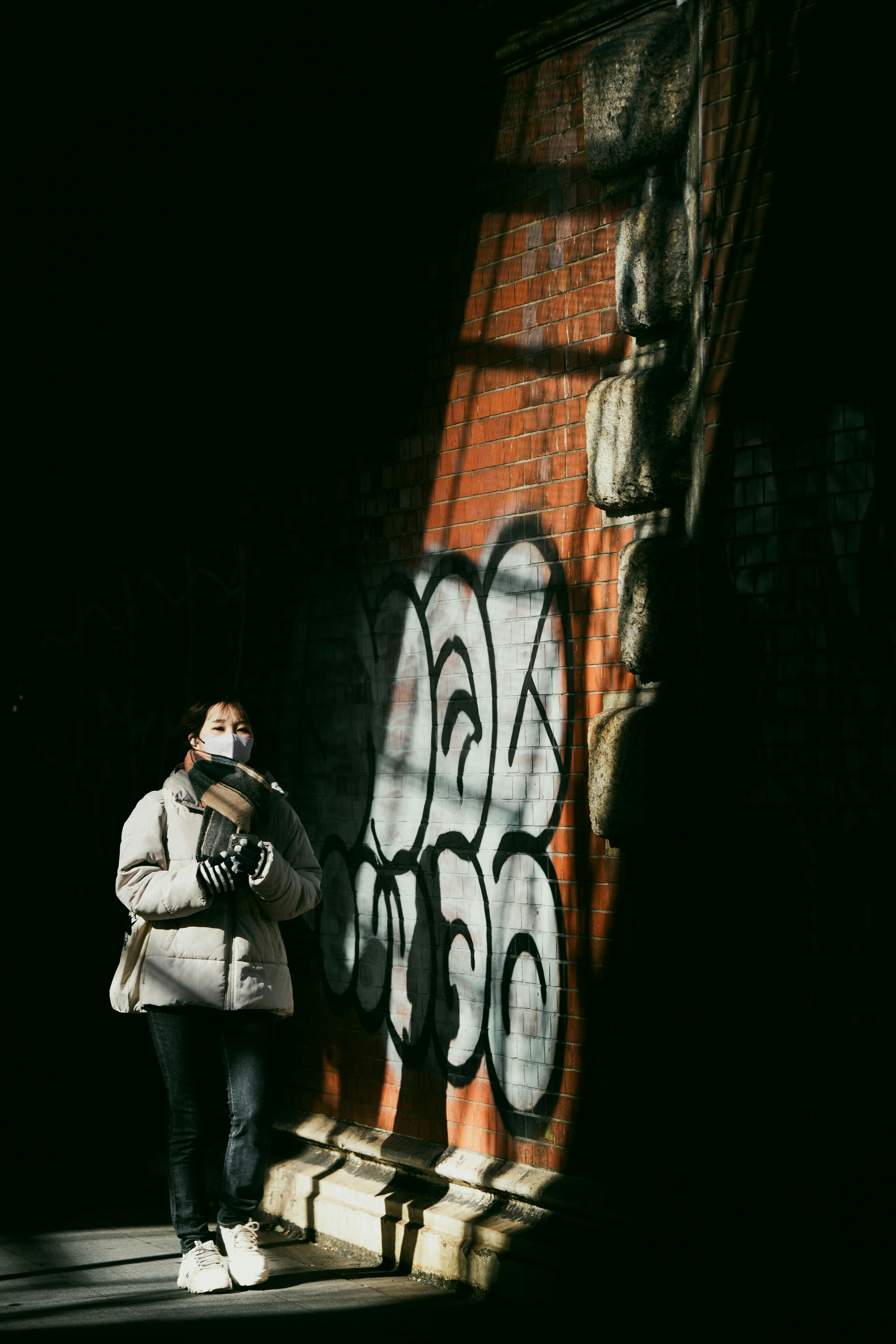 Gratis En person står ved en graffitidekket vegg i Tokyo, Japan, under dramatiske skygger. Arkivbilde