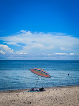 A vibrant beach scene featuring a colorful umbrella and a calm blue sea under a clear sky.