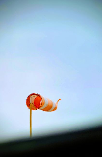 Fotomural Brillante viento naranja indicando la dirección del viento contra un cielo azul claro.