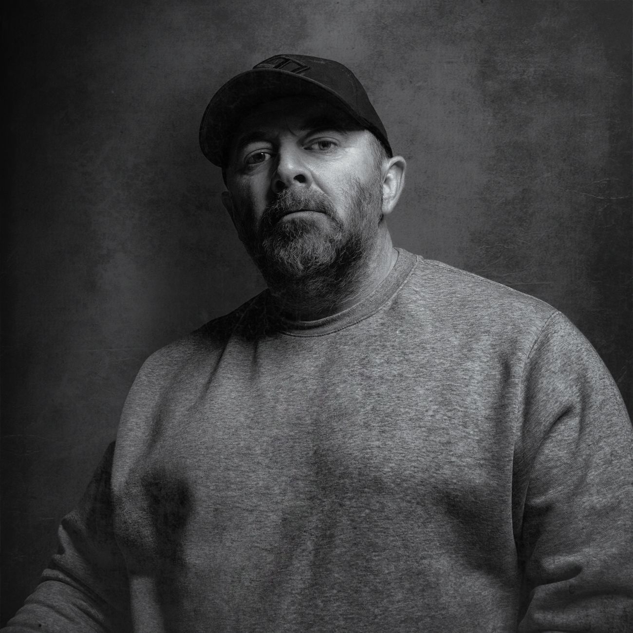 Black and white portrait of a man in a casual sweater and cap.