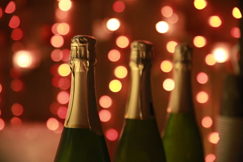 Foil-capped sparkling bottle necks lit by string lights — photo by Moran Avni on Pexels