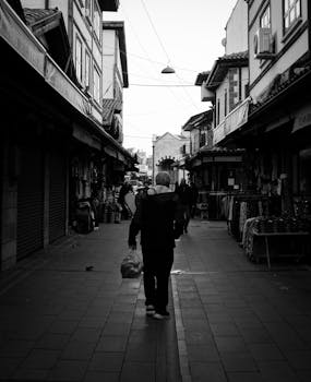 A monochrome photo capturing a person walking through a historic market alley, showcasing architecture.