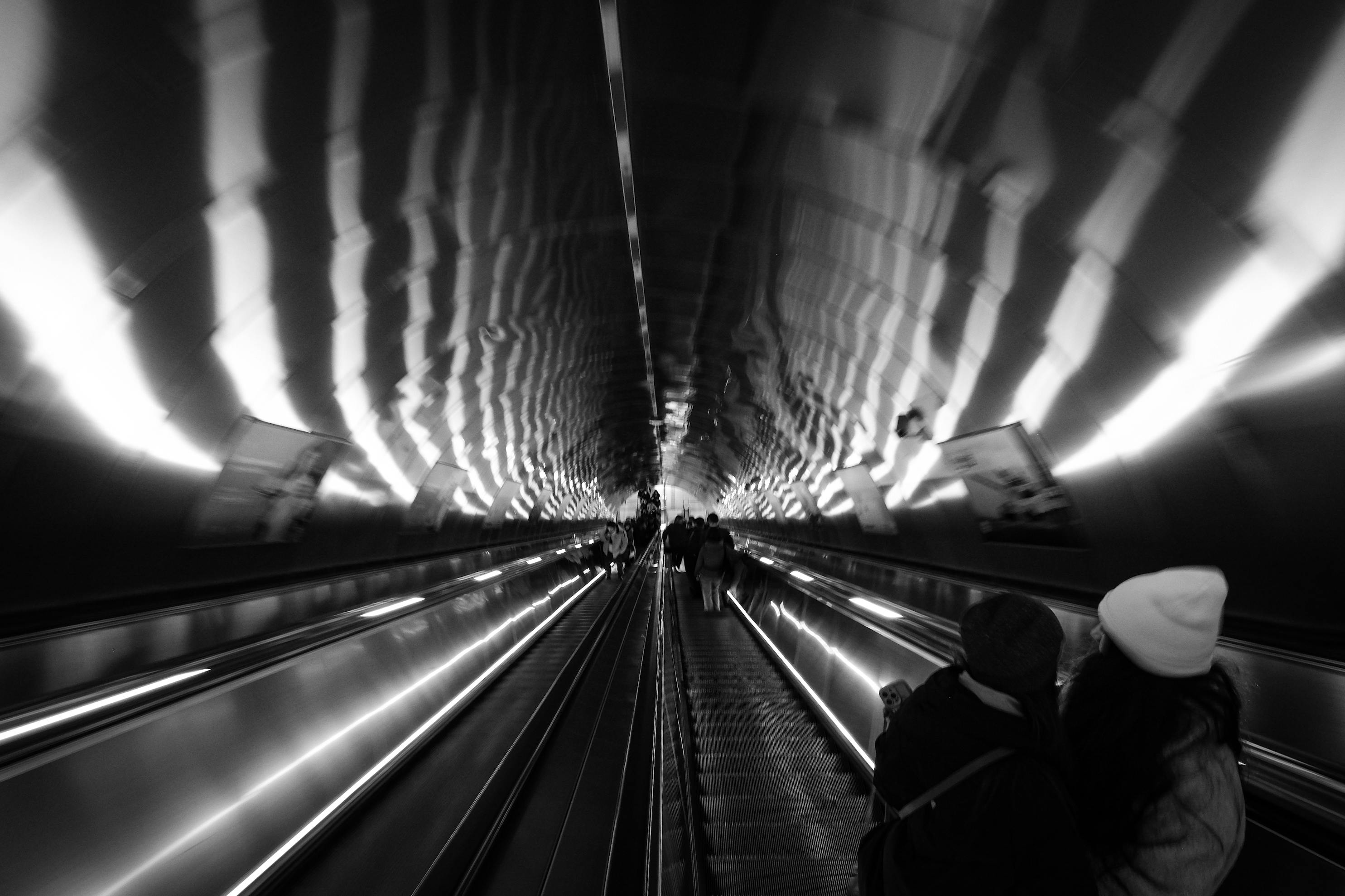 Free Dramatic black and white photo of a subway escalator with people ascending. Stock Photo