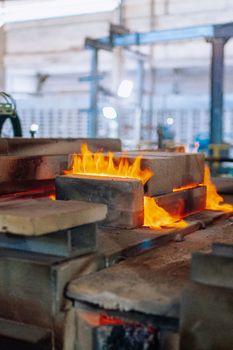 Flames rise around molds in a glass factory, showcasing industrial glass manufacturing.