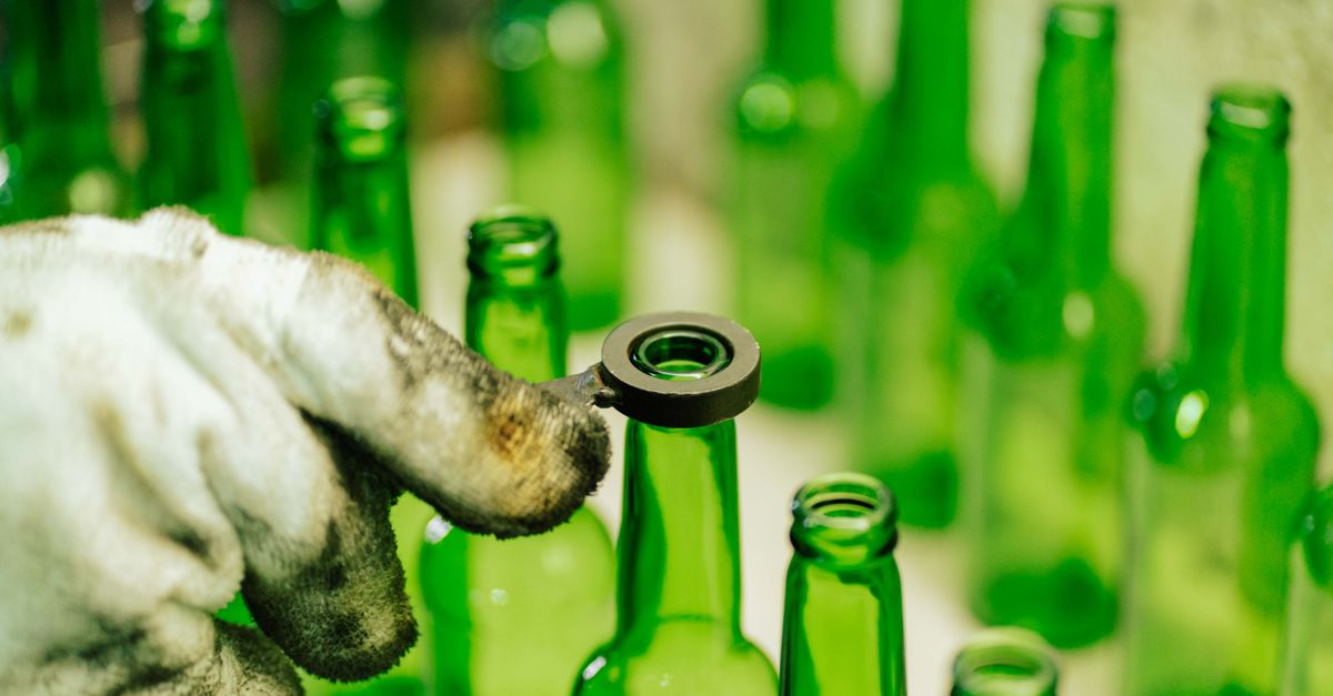 Close-up of a worker handling green glass bottles in a factory setting in Tanzania.