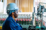 Industrial factory worker with a hard hat supervises glass bottles on an assembly line.