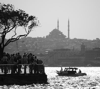Black and white view of Istanbul with fishermen on the shore and a boat on the Bosphorus.