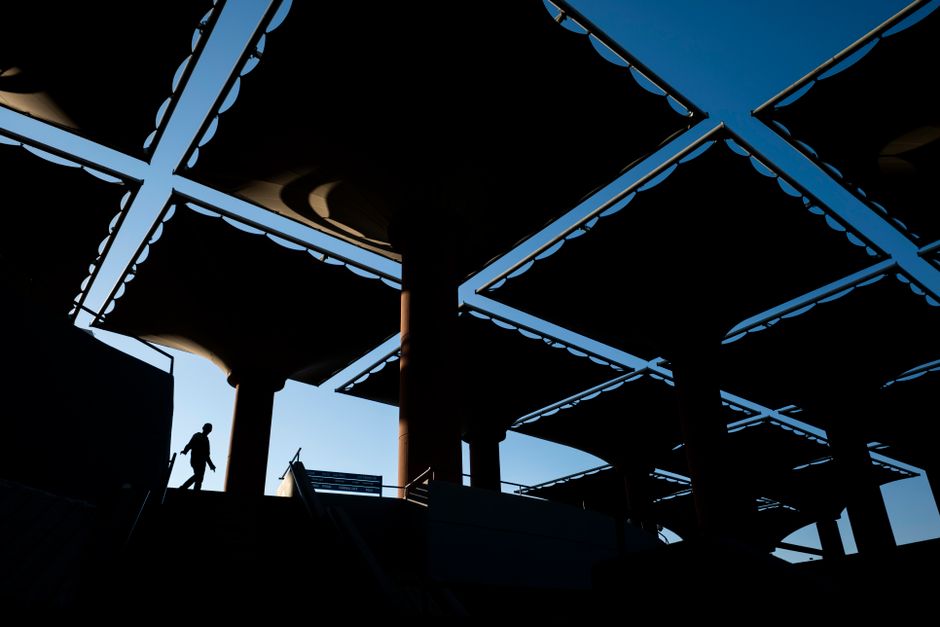 A silhouette of a person walking under a geometric canopy structure with a striking sky background.