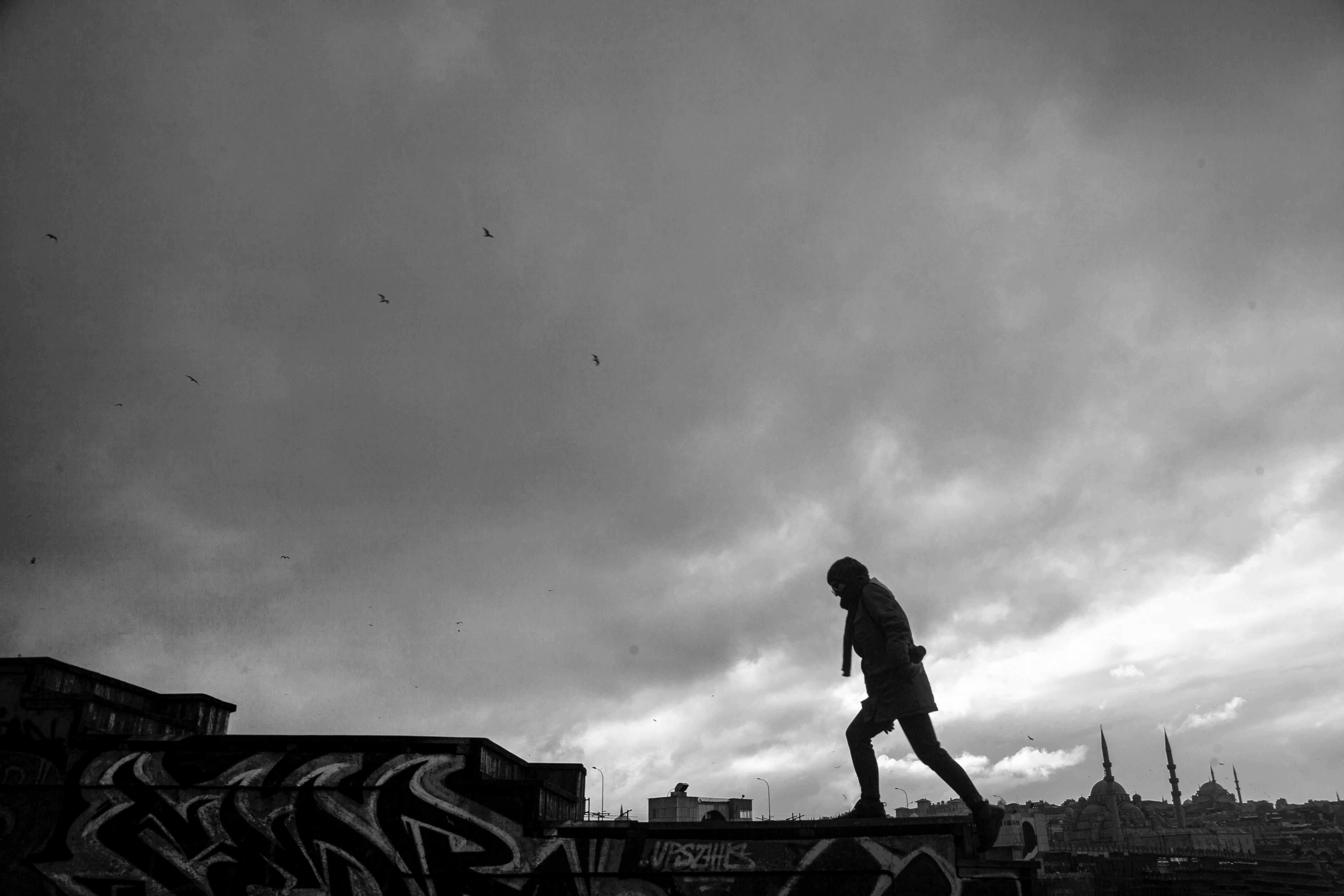 Gratis Dramatisk svart-hvitt-silhuett av en mann som går på et graffitidekt tak under overskyet himmel. Arkivbilde