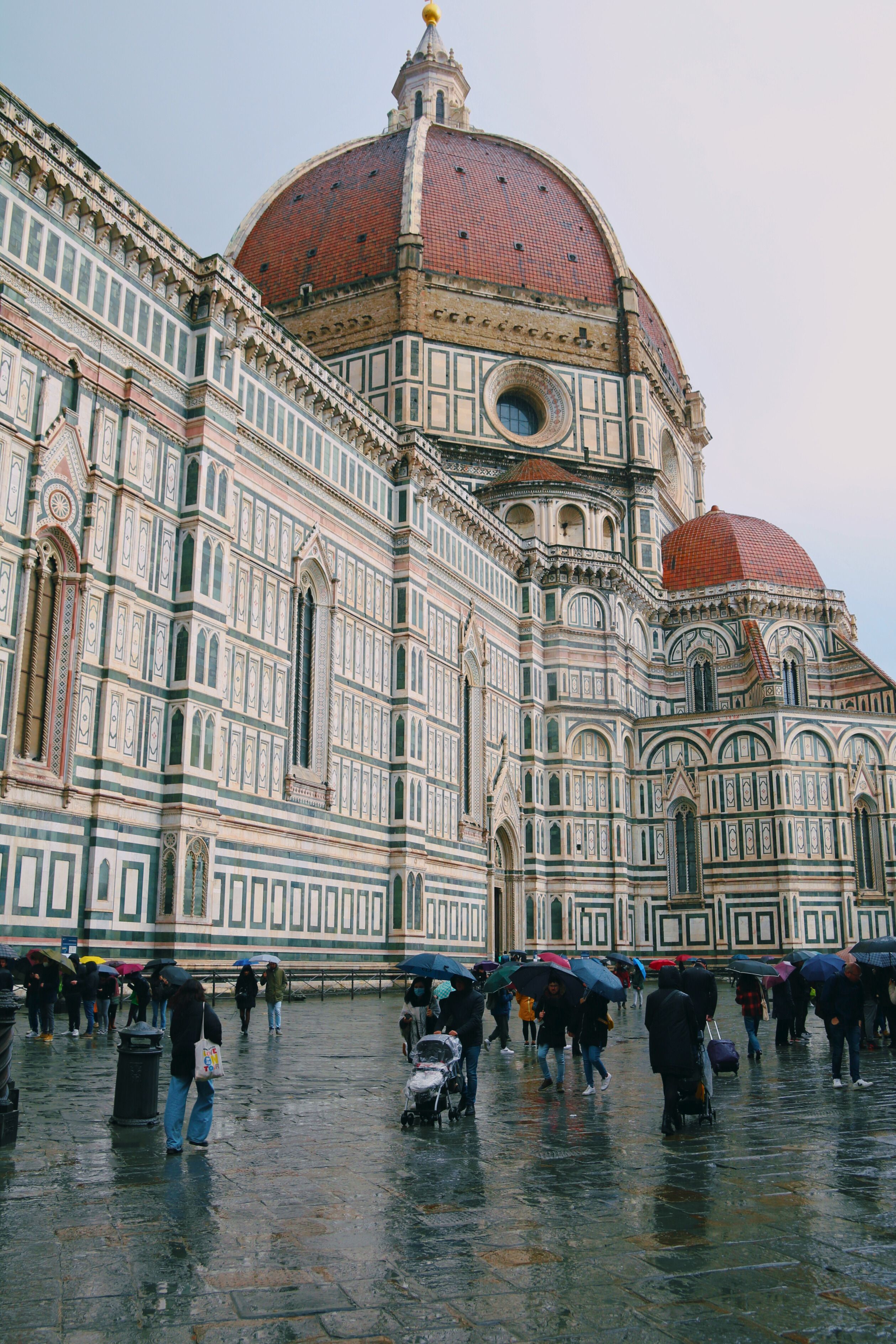 Florence Cathedral dome and facade on a rainy day with people and umbrellas.