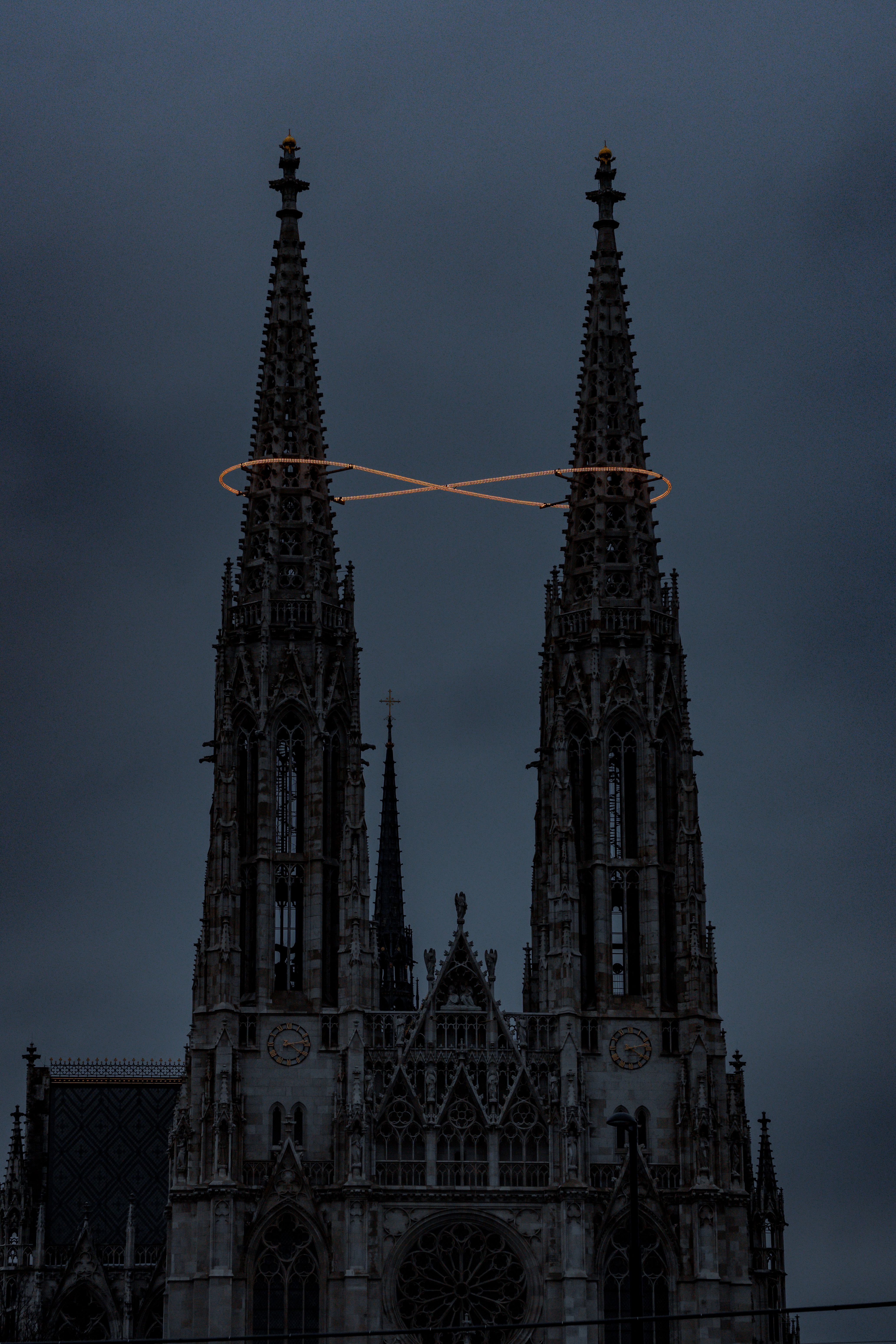 Dramatic view of Vienna's Votivkirche spires with halo lighting at dusk. Captivating Gothic architecture.