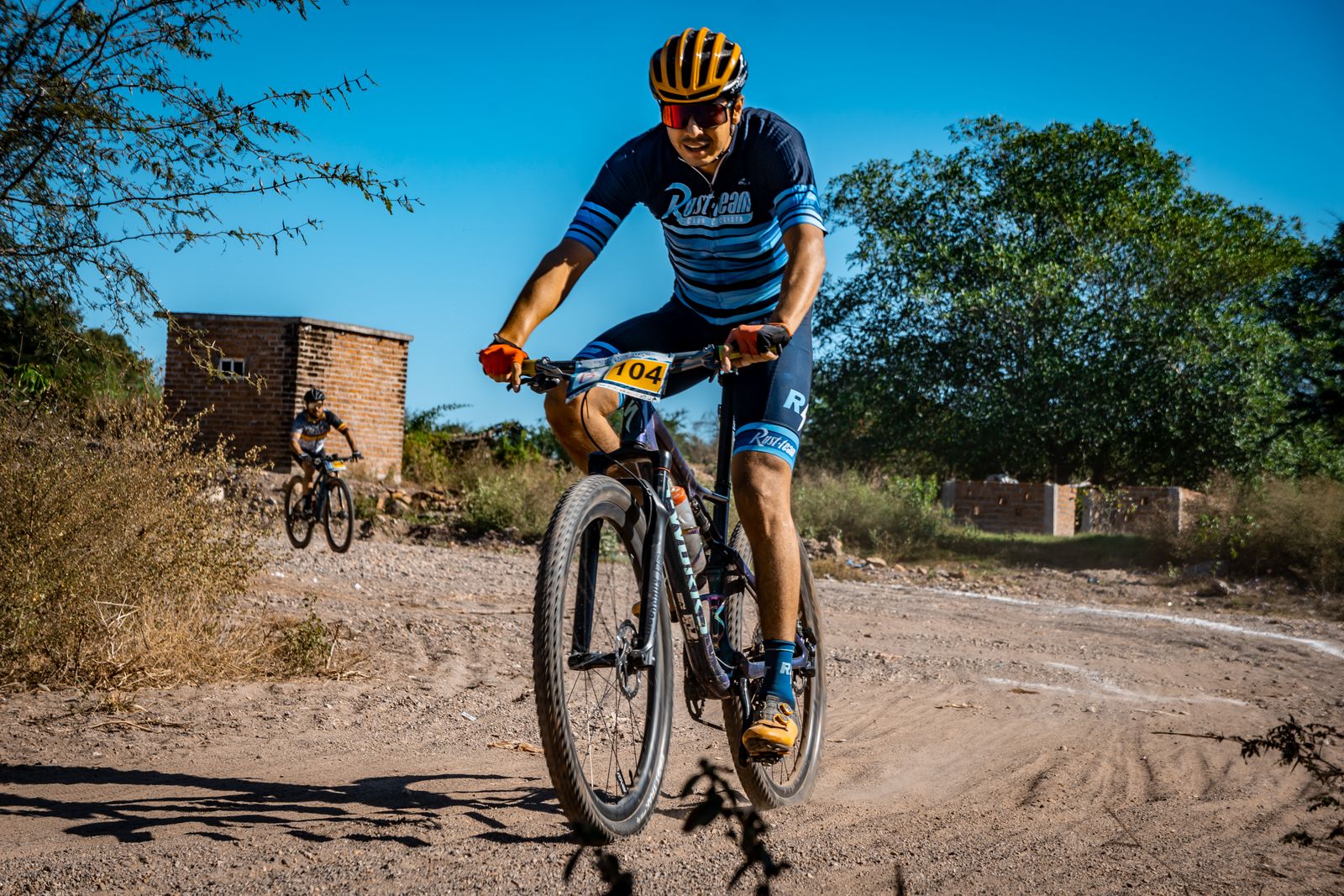 Gravel cyclists riding a dusty dirt road under a clear blue sky on gravel bikes
